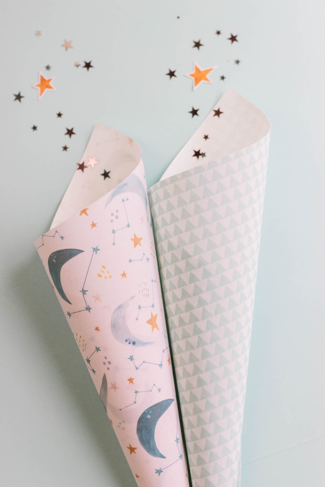 Dois rolos de papel de embrulho com padrões de luas e triângulos sobre superfície cinza