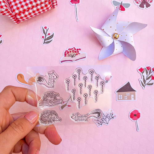 Cartela de autocolantes transparentes com desenhos em preto e branco segurada por mão sobre fundo cor-de-rosa com autocolantes de flores