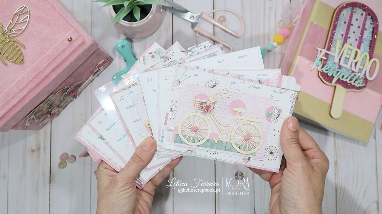 Cartões decorativos com bicicleta e balões em mãos, caixa rosa, ferramentas e bloco de notas com palavra FELIZ