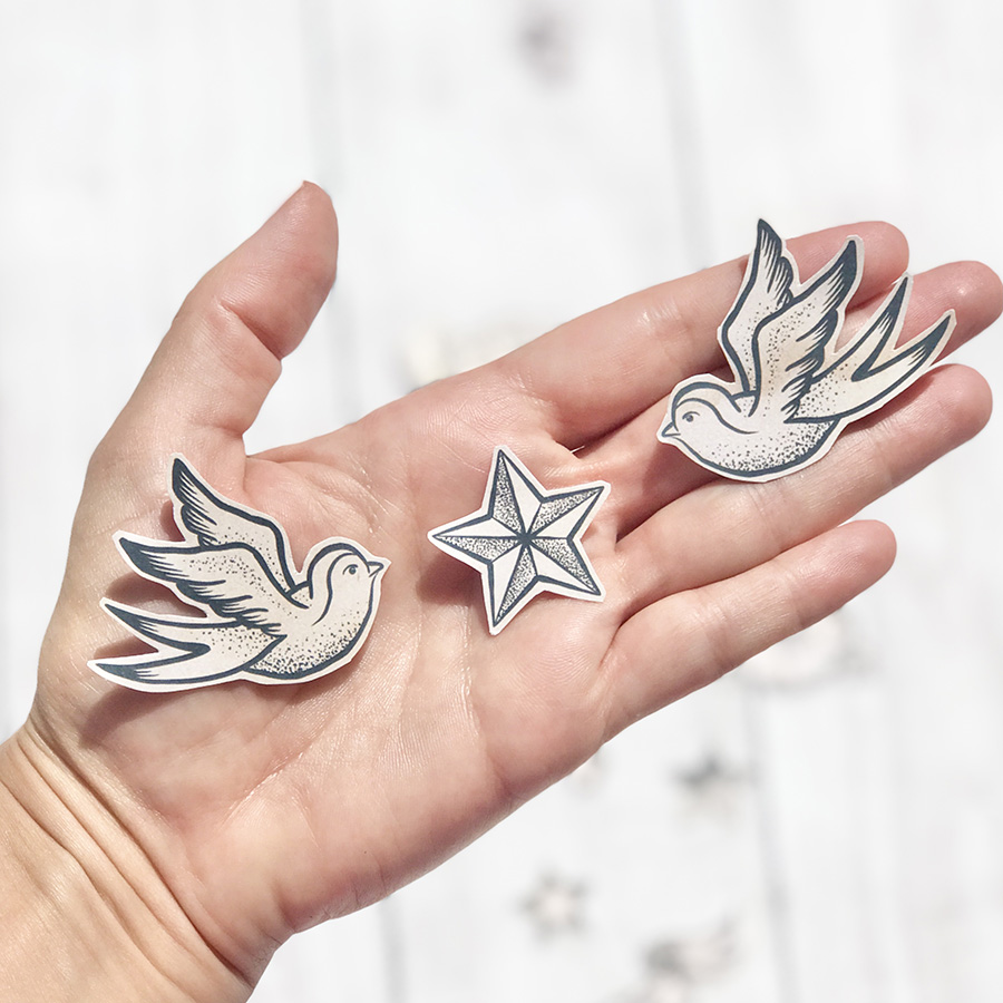 Figuras de papel preto e branco de aves e estrela numa mão com fundo branco desfocado