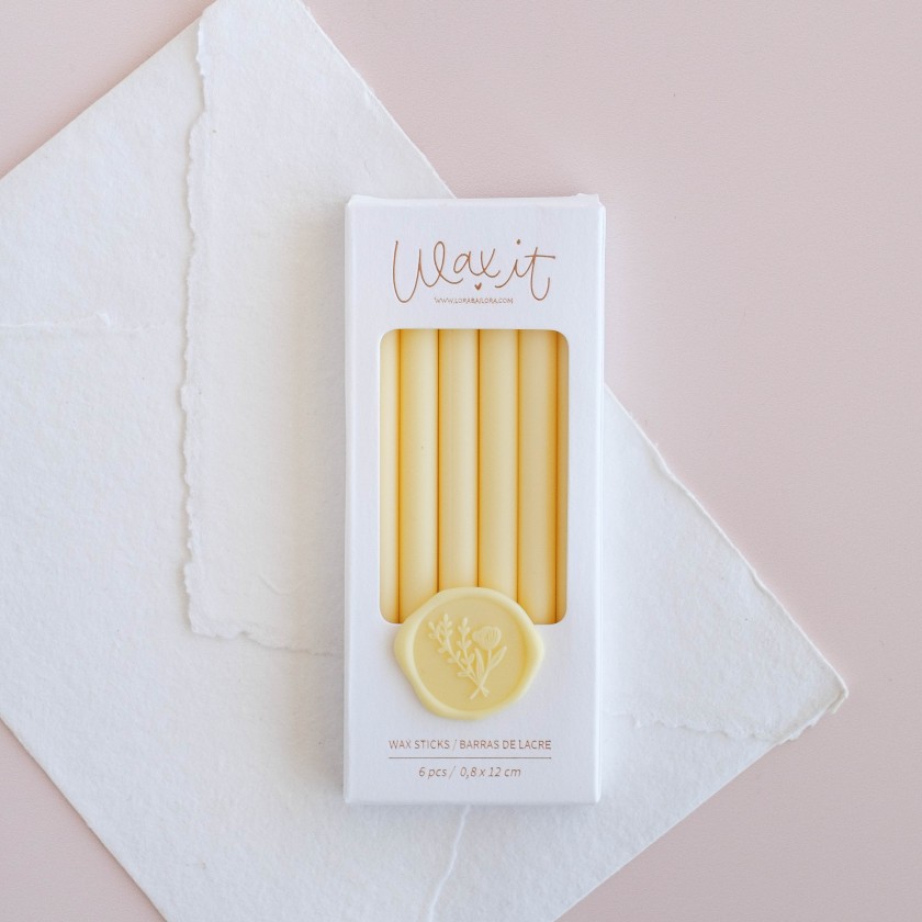 Palitos de lacre amarelos na embalagem branca sobre papéis brancos e fundo rosa