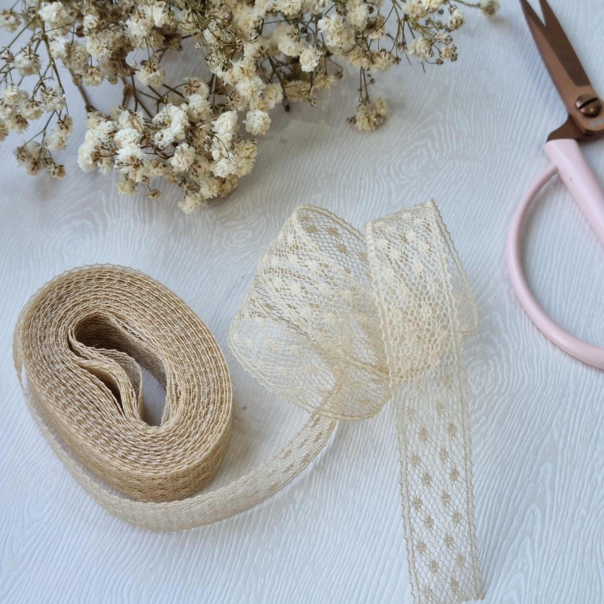 fitas de juta e renda com flores secas e tesoura rosa sobre fundo branco texturizado