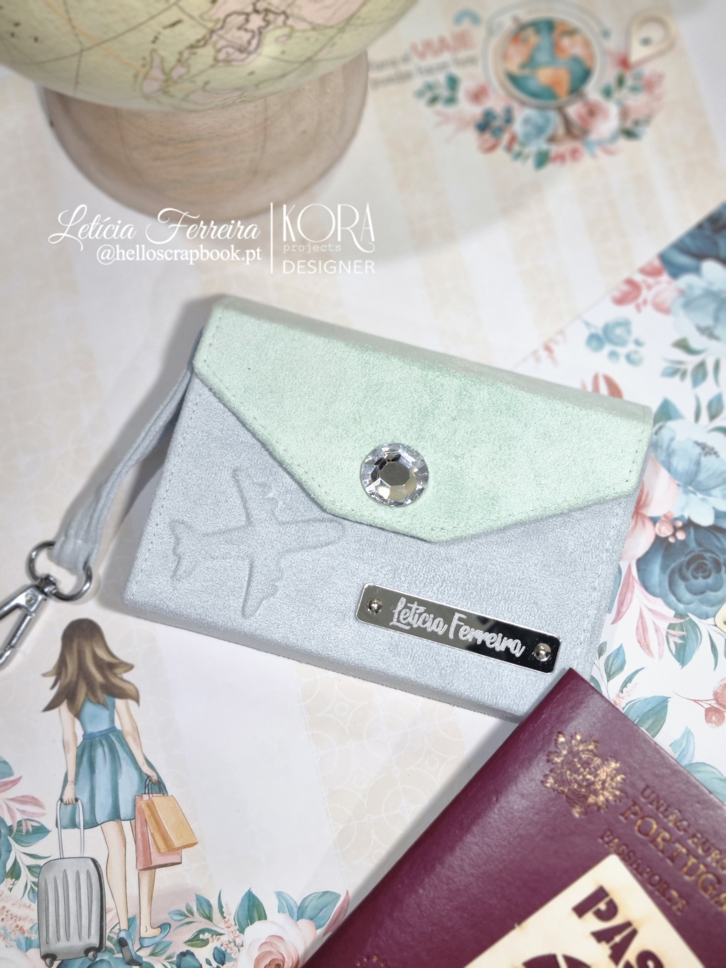 Carteira decorativa verde água e cinza com botão brilhante e etiqueta Letícia Ferreira junto a passaporte e ilustração.