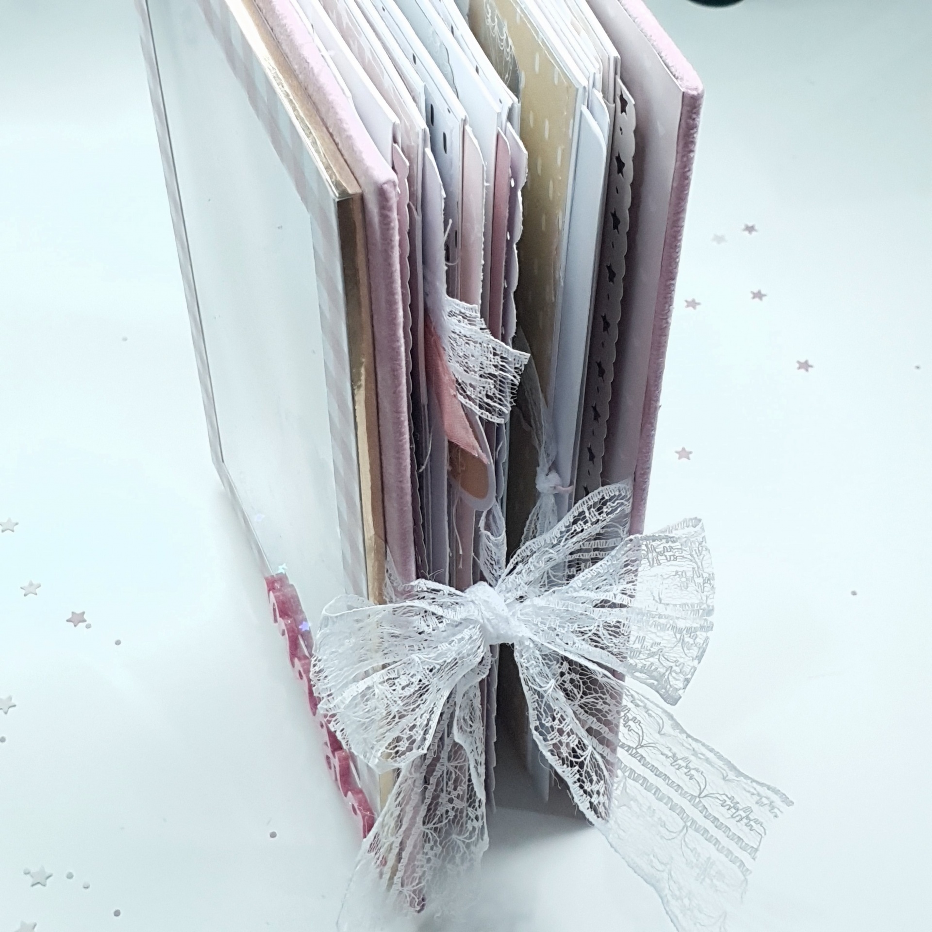 álbum de fotos decorado com laço de renda e páginas variadas sobre fundo branco com estrelas