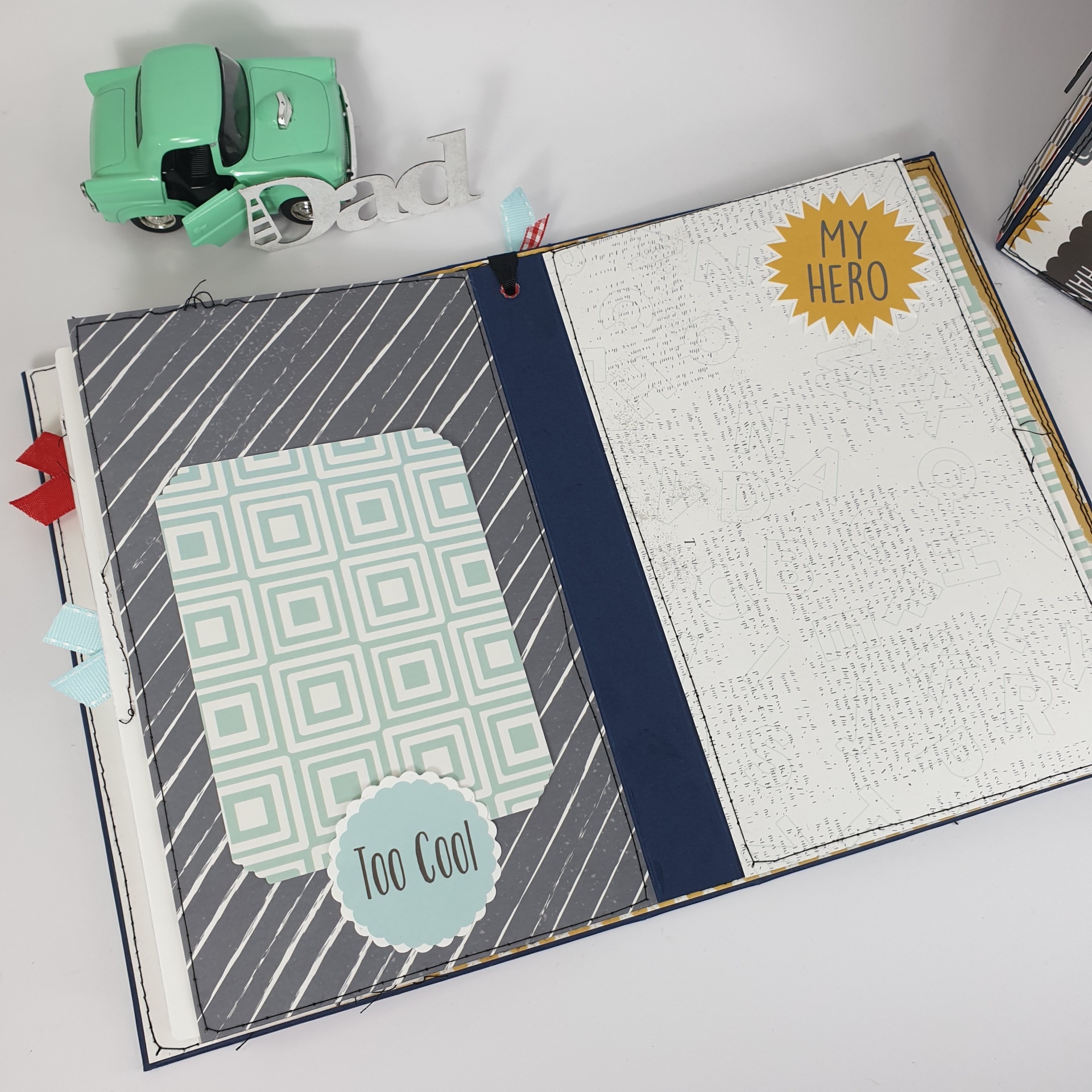 Livro aberto decorado com etiquetas 'Too Cool' e 'MY HERO', carro verde vintage e palavra prateada 'Dad'