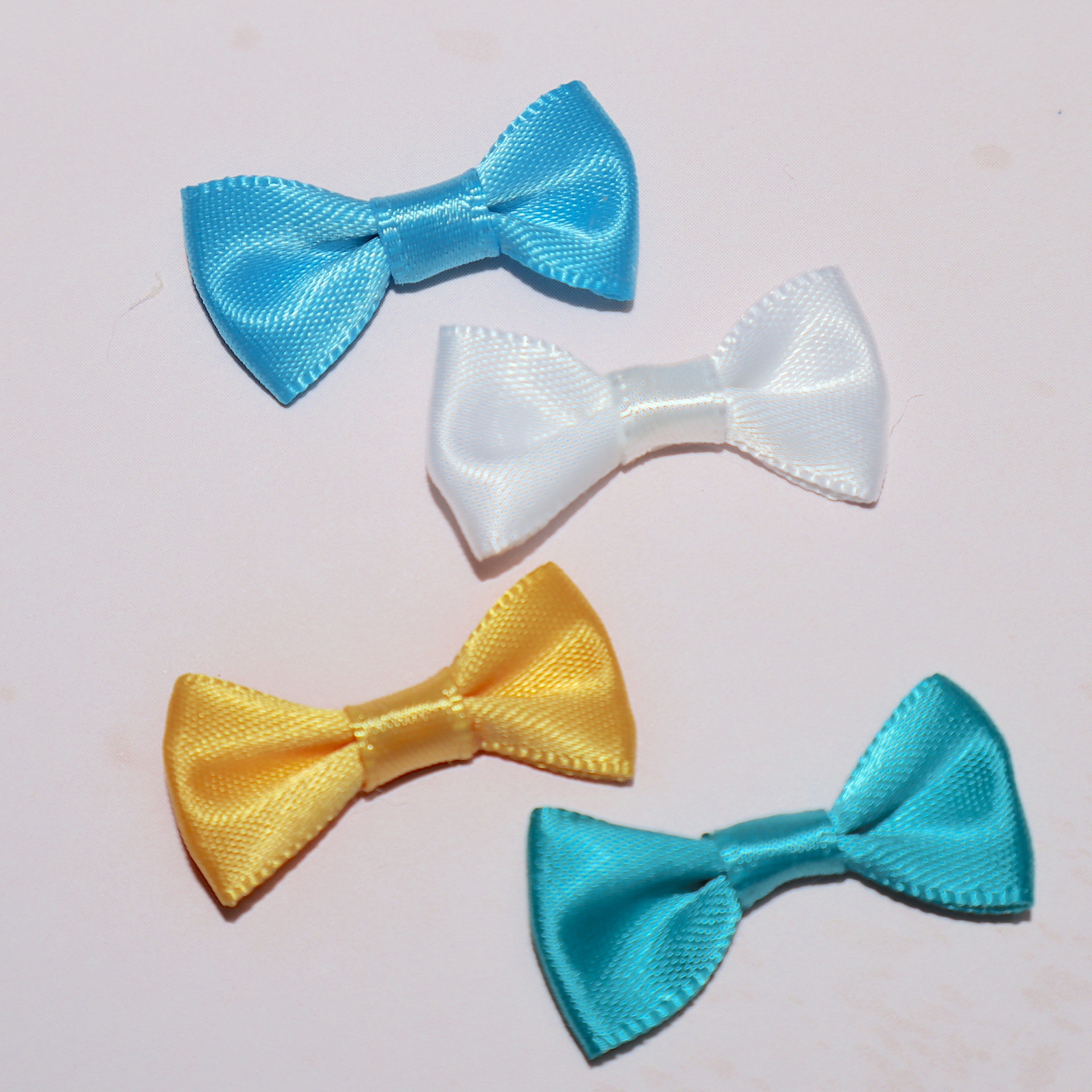 Quatro pequenos laços de fita coloridos em cetim sobre fundo branco