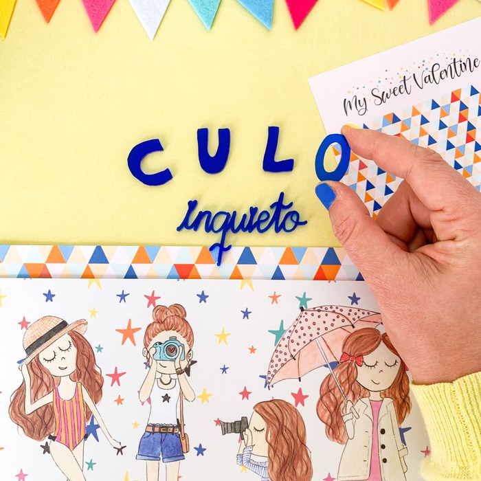 Palavras em feltro azul sobre fundo amarelo com ilustrações e mão a segurar uma letra.