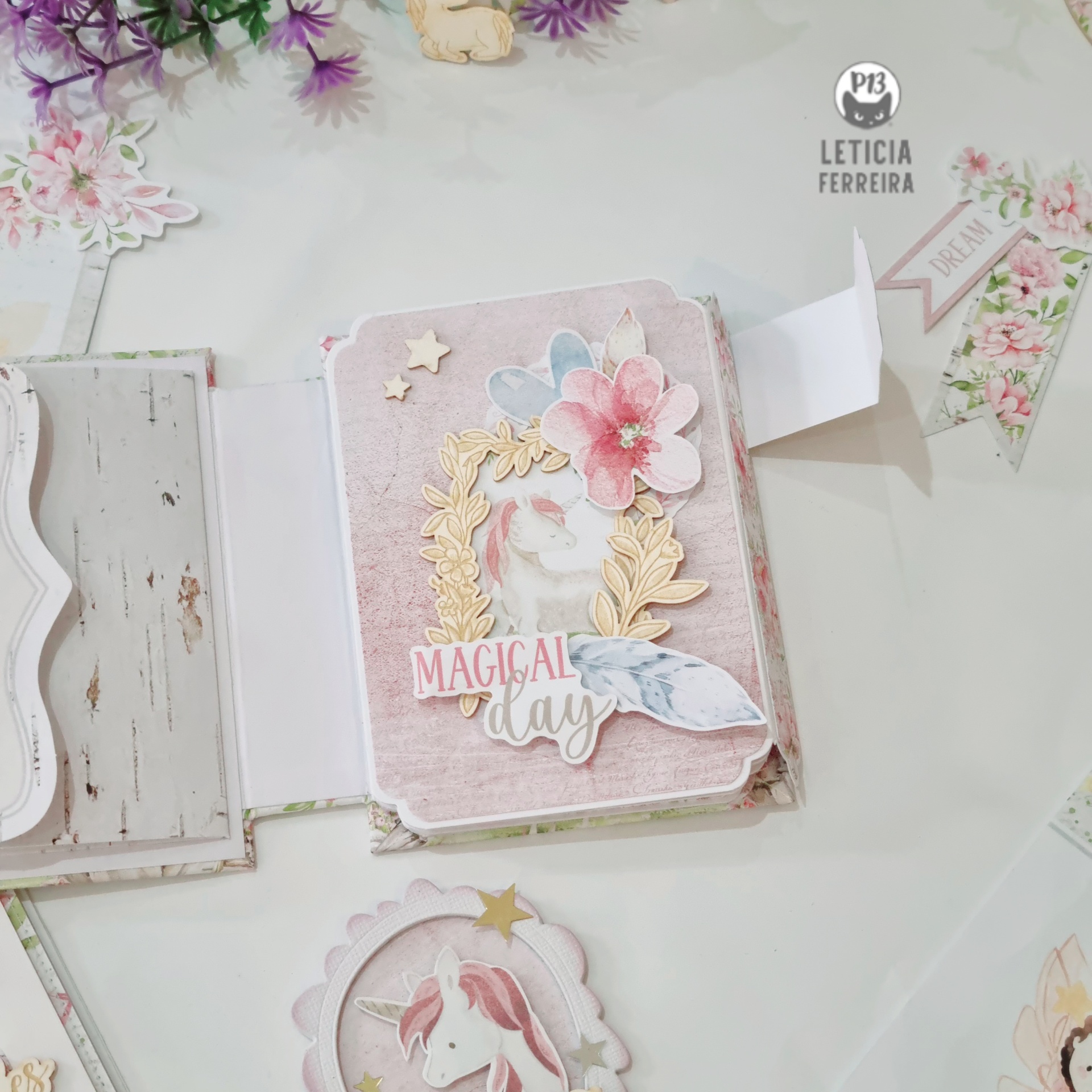 Mini álbum decorado com flores de papel e moldura dourada, com texto 'MAGICAL day' em fundo pastel