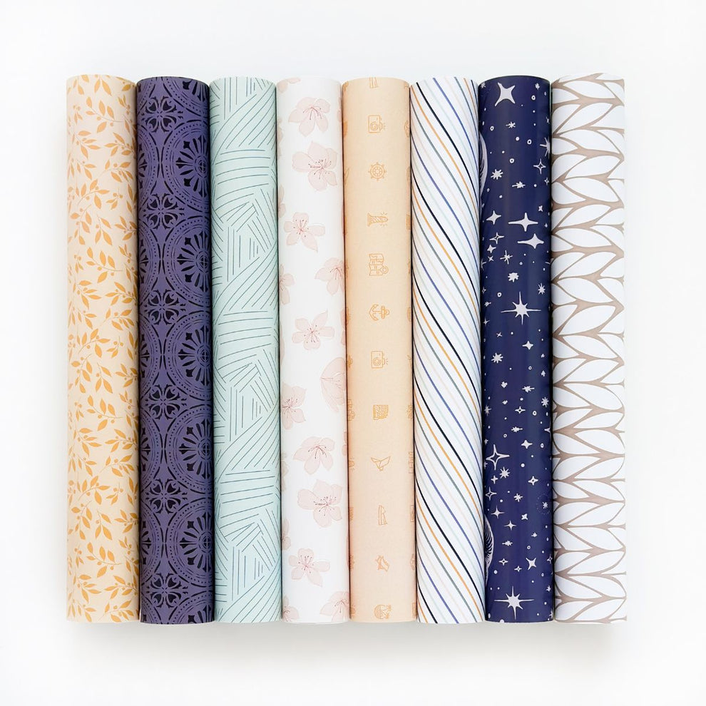 Oito rolos de tecido com vários padrões e cores sobre fundo branco.