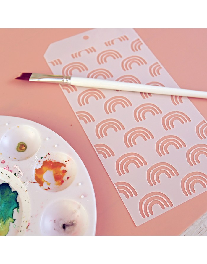 Paleta de pintura com tintas, pincel branco e molde com padrão de arcos cor de rosa sobre mesa rosa.