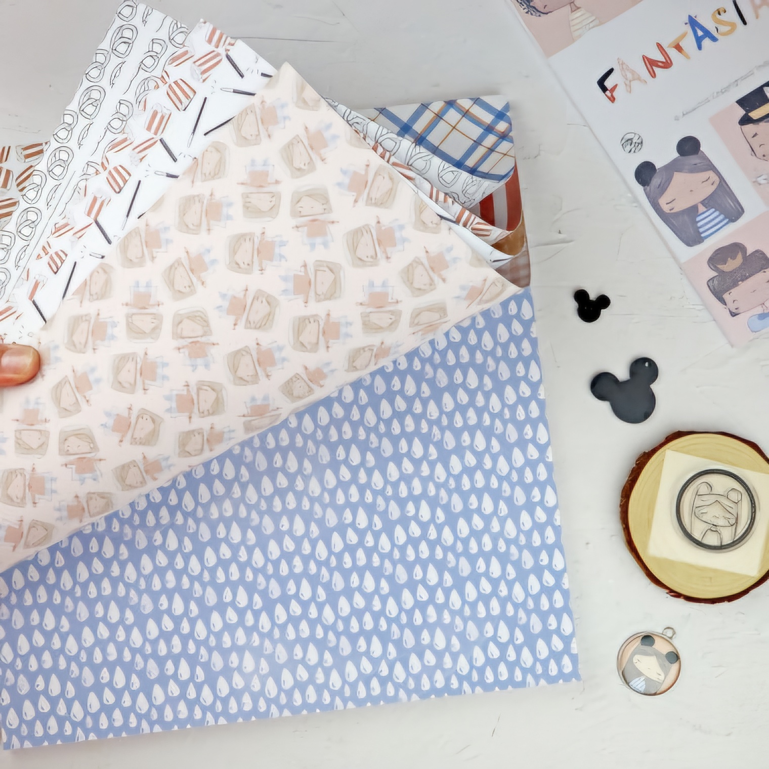 Folhas de papel decorativo com vários padrões coloridos sobre mesa branca e objetos decorativos.