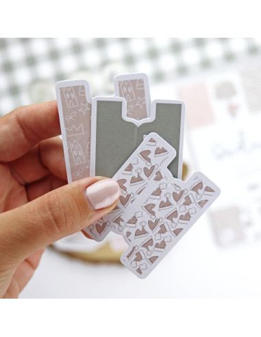 Marcadores de página magnéticos com padrões ilustrativos em bege e castanho nas mãos.