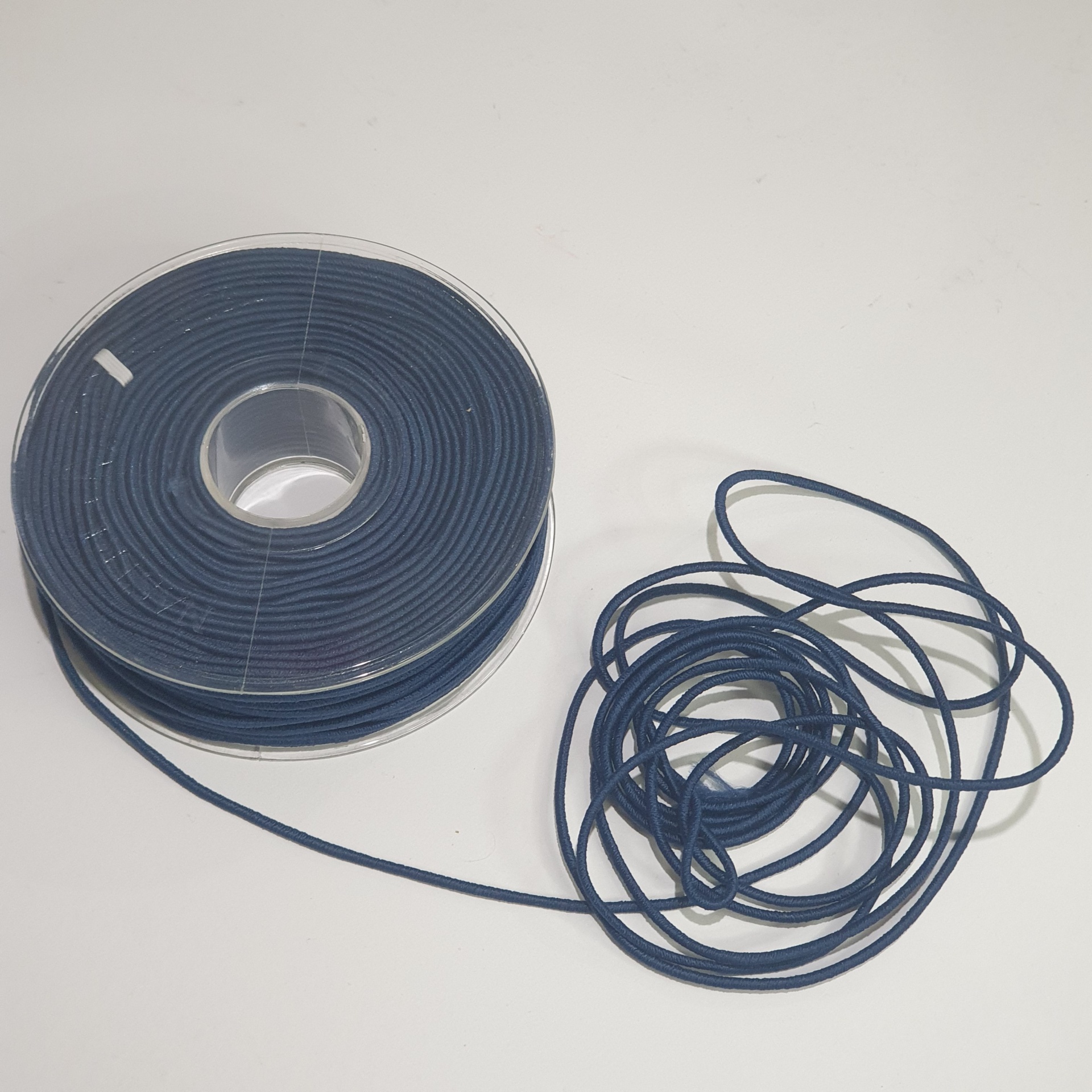 Rolo de fio azul escuro parcialmente desenrolado em superfície branca