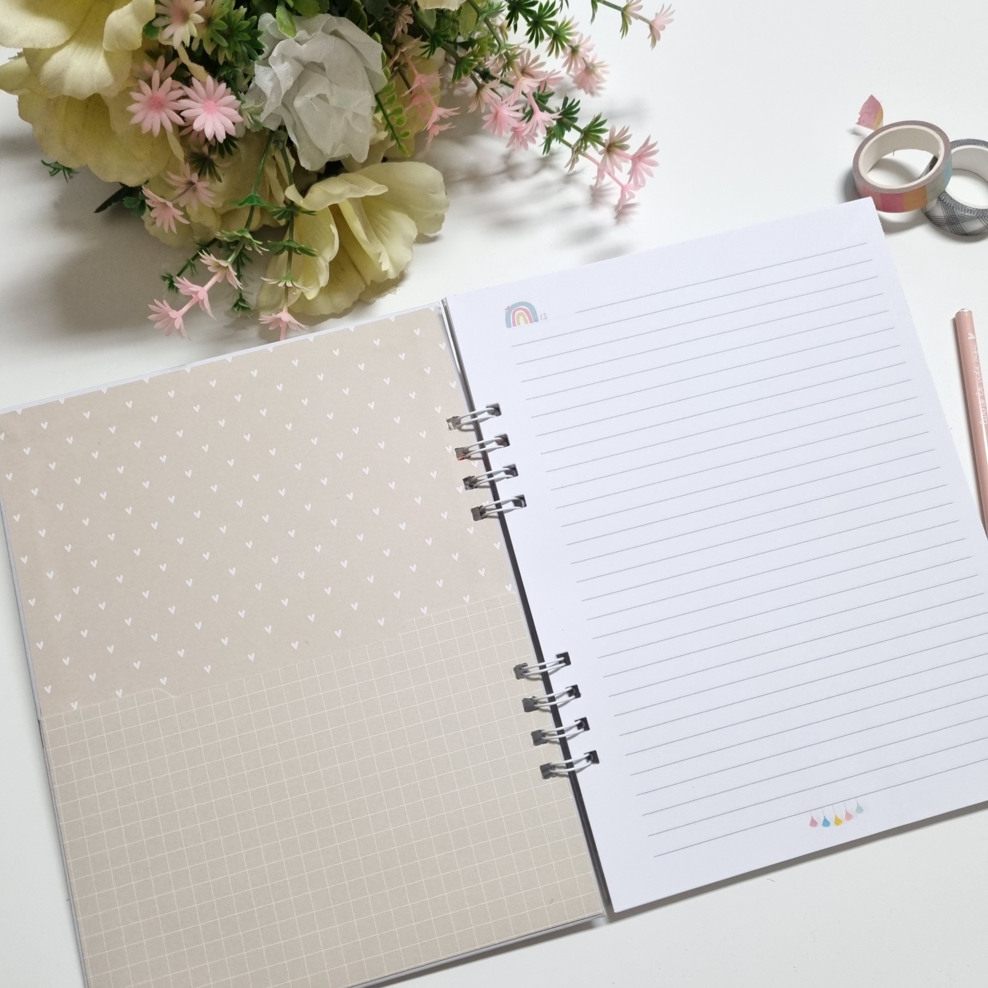 Caderno aberto com capa interna bege com padrões brancos e páginas pautadas, com flores e material de escrita ao lado