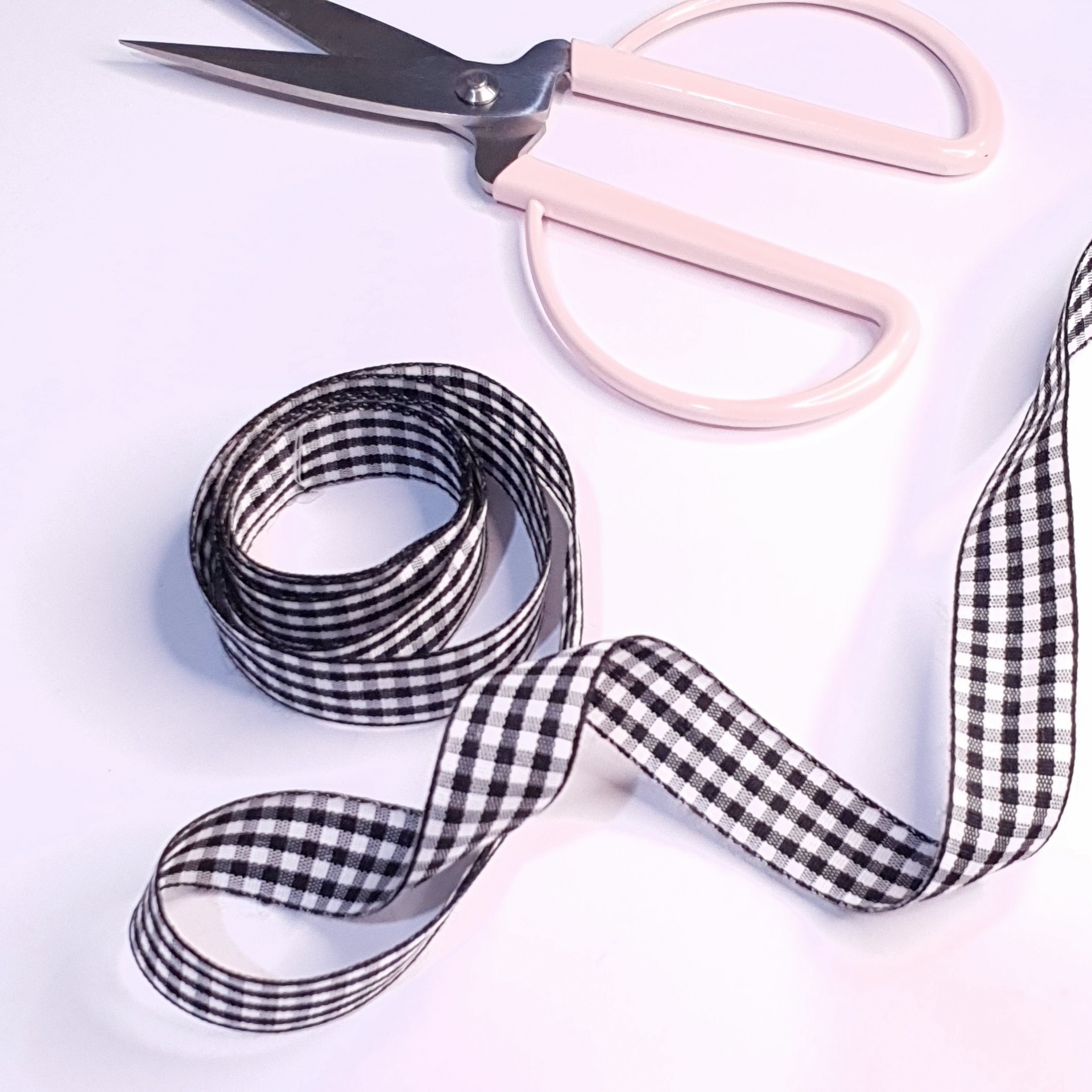 Tesoura rosa claro e fita xadrez preto e branco sobre fundo branco
