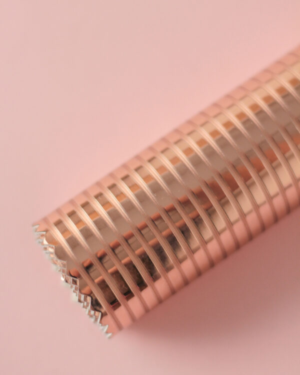 Rolo de papel de embrulho metálico cobre com padrão de riscas sobre fundo rosa