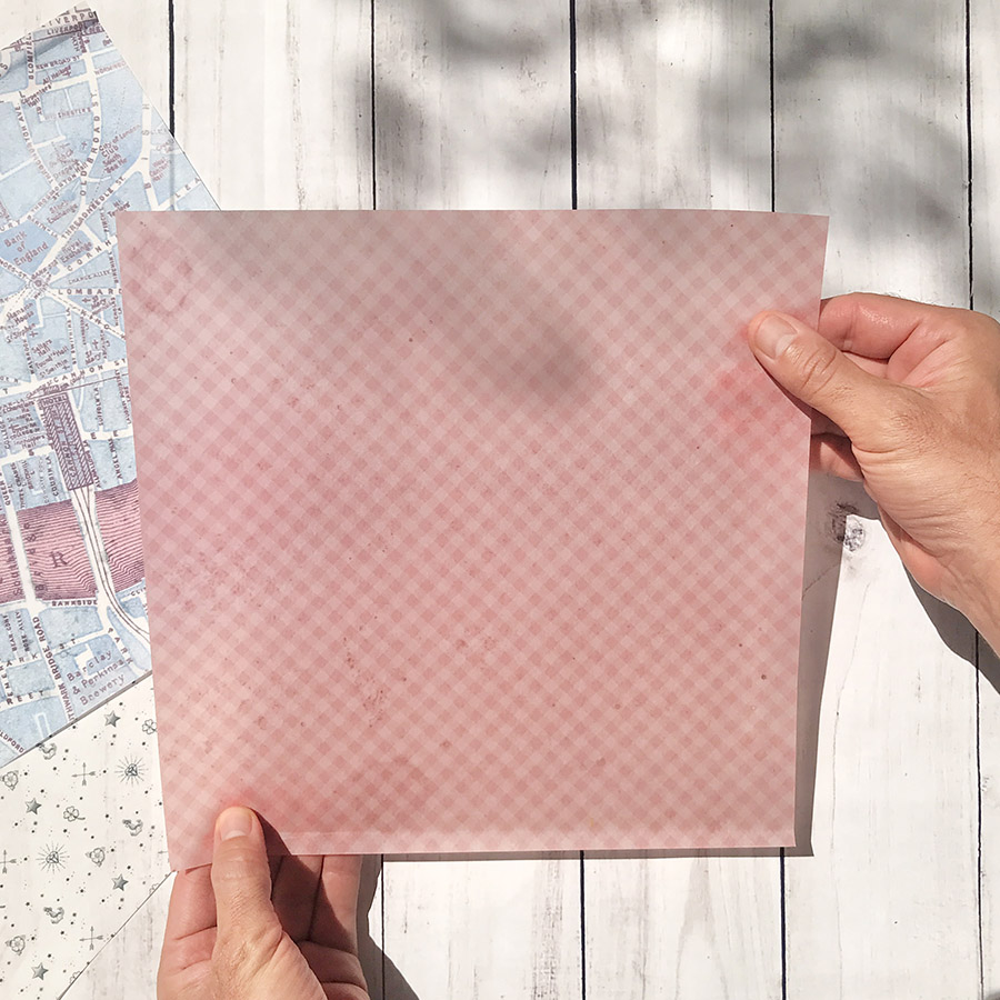 Folha de papel rosa xadrez segurada pelas mãos sobre mesa branca de madeira