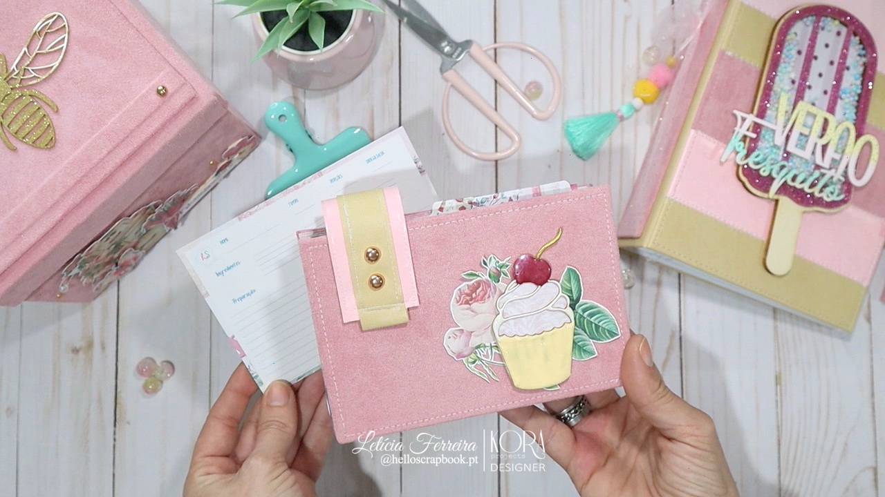 Carteira rosa com decoração de cupcake e agenda com tema de gelado sobre mesa de madeira