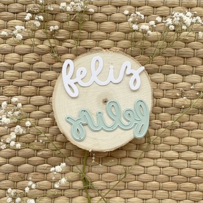 Disco de madeira com palavras decorativas felizes e grilo sobre tecido trançado com flores brancas.