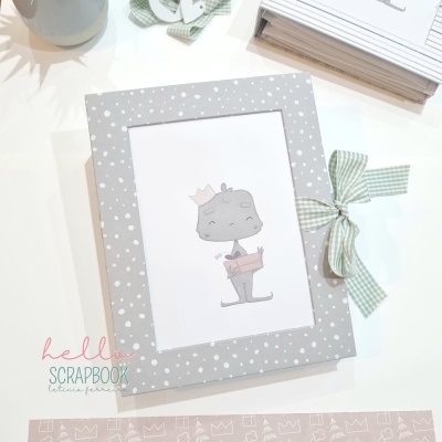 Álbum de scrapbook cinza com bolinhas brancas e personagem desenhado, perto de fitas e uma planta.