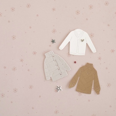 Três camisolas decorativas sobre fundo rosa com padrão de flocos de neve