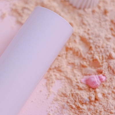 Recipiente branco em superfície com pó bege e concha rosa