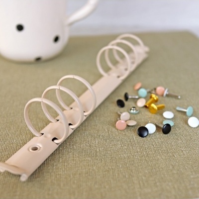 Anilha branca metálica com tachos coloridos ao lado sobre tecido verde.