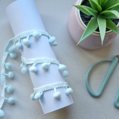 Fita decorativa com pompons enrolada, planta e cabide sobre mesa branca