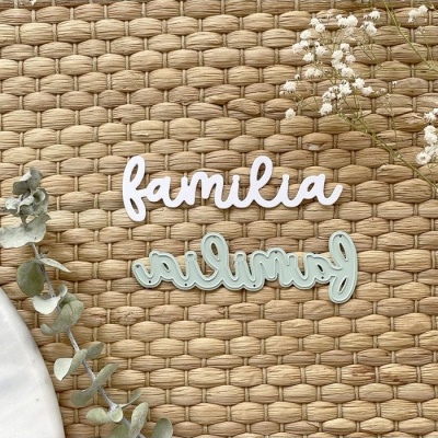 Duas palavras decorativas 'familia' em branco e azul claro sobre esteira de palha com folhas e flores secas