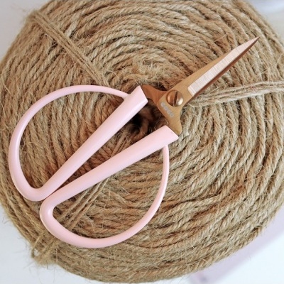 Tesoura pequena com cabos rosa claro sobre novelo de corda rústica