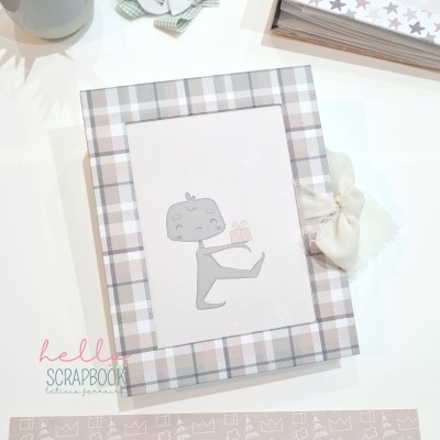 Livro scrapbook com capa xadrez bege e branca e personagem ilustrado segurando presente
