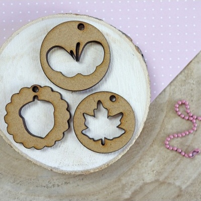 Três etiquetas decorativas de madeira com recortes variados sobre base de madeira clara