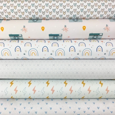 Tecidos com padrões variados de corações, câmeras, arcos-íris, pequenas cruzes e relâmpagos em tons de cinza, azul, laranja e terracota.