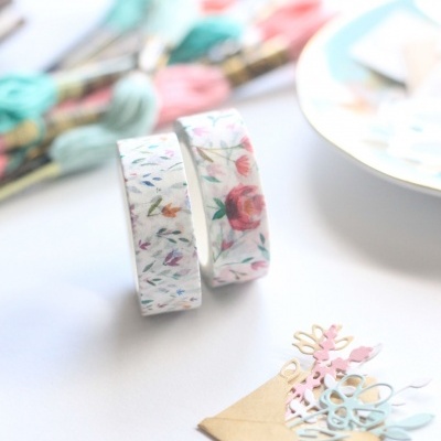 Rolos de fita washi florais, pequena bolsa de papel com recortes e meadas de linha colorida
