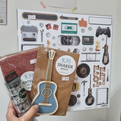 Mãos segurando botões de metal Sizzix e cartão com guitarra KORA projects SHAKER guitarra, com poster de objetos retro ao fundo.