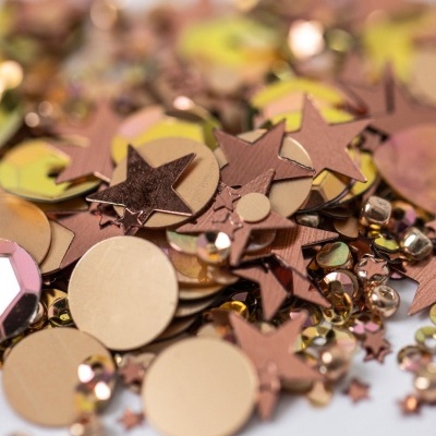 Lantejoulas douradas, cobre e bronze em várias formas sobre fundo claro