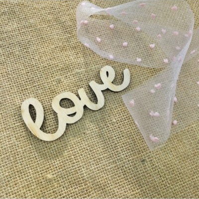 Peça decorativa em madeira com a palavra 'love' sobre tecido de juta e tecido transparente com pompons cor-de-rosa