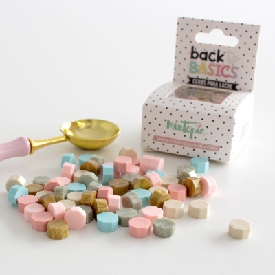 Ceras para lacre multicoloridas em fundo branco com colher dourada e caixa branca pontilhada