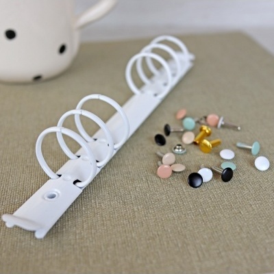 Argolas metálicas brancas para fichários junto a rebites coloridos sobre superfície castanha