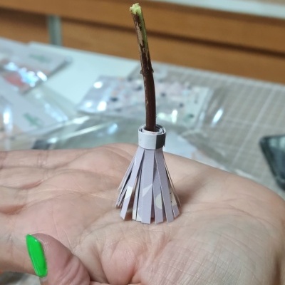 Mão segurando pequeno objeto artesanal de papel e ramo de madeira.