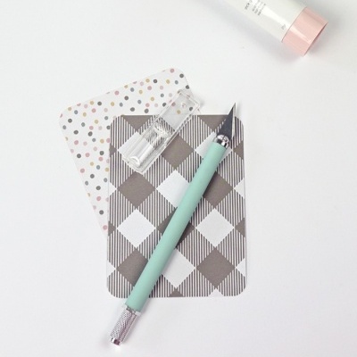 Cortador de unhas azul-claro sobre cartões decorados e tubo branco com tampa rosa