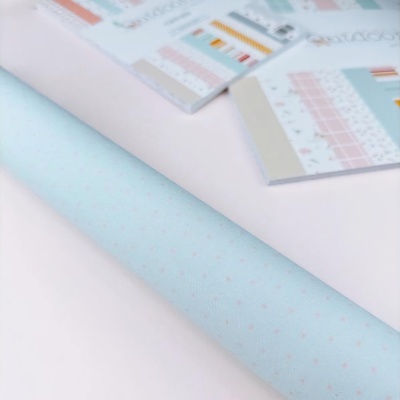 Rolo de papel azul claro com estrelas rosas ao lado de folhas de amostras coloridas sobre mesa branca