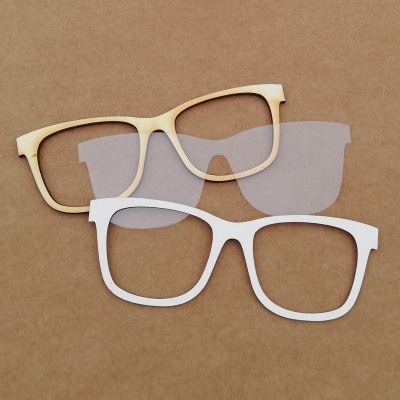 Dois armações de óculos sem lentes, uma em madeira clara e outra branca, sobre fundo castanho.