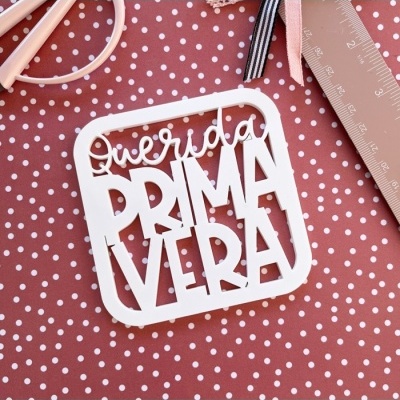 Etiqueta decorativa branca com texto 'Querida PRIMAVERA' sobre tecido castanho com bolinhas brancas
