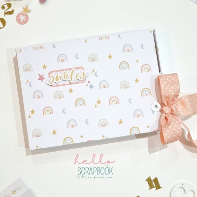 Livro de scrapbooking branco com desenhos de arco-íris, estrelas, luas e laço cor-de-rosa