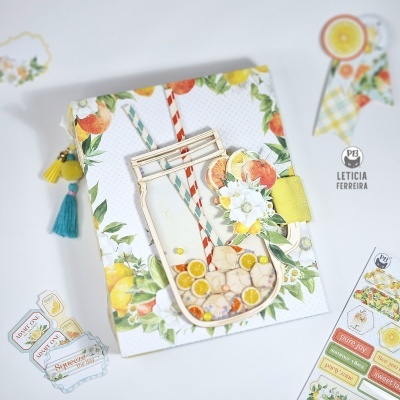 Caderno com decoração de frutas cítricas e jarra acrílica, rodeado por adesivos coloridos.