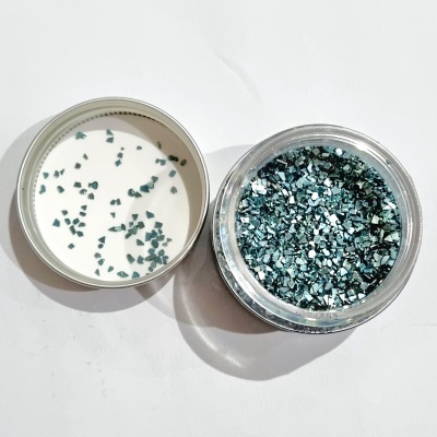 Frasco pequeno com pedaços brilhantes verde-azulados e tampa removida