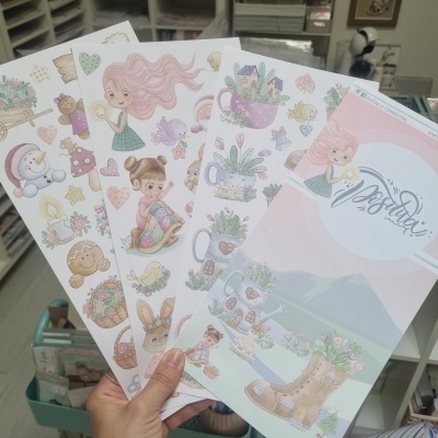 Cartões decorativos com ilustrações infantis em tons pastel segurados por uma mão
