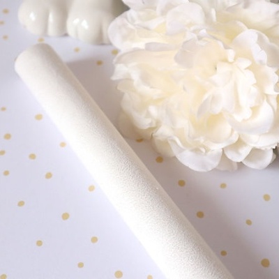 Vara branca texturizada junto a flor artificial branca sobre fundo branco com pontos dourados