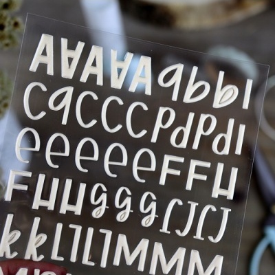 Folha transparente com letras recortadas em branco em vários estilos e tamanhos.